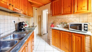 A kitchen with wooden cabinets, a stainless steel sink, a microwave, and a red kettle.