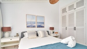 A bedroom with a bed, two bedside tables, a nightstand, a lamp, a wall-mounted picture, and a wardrobe.