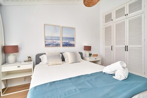 A bedroom with a bed, two bedside tables, a nightstand, a lamp, a wall-mounted picture, and a wardrobe.
