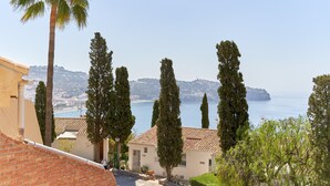 A coastal view with a building, tall trees, and a clear sky.