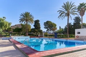 Una piscina con cubierta roja, rodeada de palmeras y un cielo azul despejado.