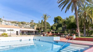 A swimming pool with steps leading into it, surrounded by palm trees and a building with a tiled roof.