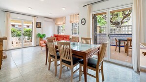 A dining area with a glass-top table and wooden chairs, a red sofa, and a view through a glass door to an outdoor patio. - Holiday Home 'Villa Jordi Y Nuri' with Private Terrace, Wi-Fi and Air Conditioning (Cambrils)