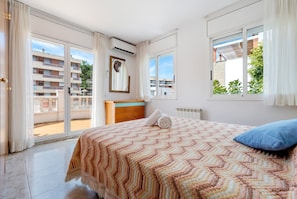 A bedroom with a bed, a window, a radiator, and a view of buildings.