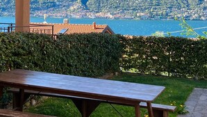 Eine hölzerne Bank in einem Garten mit Blick auf einen See und Berge.
