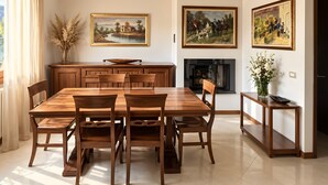 Un comedor con una mesa y sillas de madera, un jarrón con plantas secas y dos cuadros en la pared.