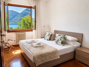 Quarto com uma janela grande, cama de madeira e vista para as montanhas.