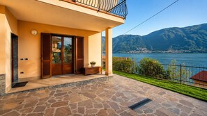A house with a stone patio, wooden doors, and a view of a lake and mountains. - Vacation Home “Charming House on the Lake” with stunning Lake View (Lezzeno)