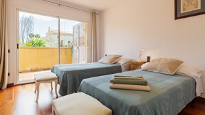 A bedroom with two beds, a small stool, and a balcony with a view of buildings. - Country House with Garden, Near Barcelona and with Sea Views (Sant Andreu de Llavaneres)