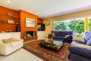 A living room with a sofa, armchair, coffee table, fireplace, and large windows.