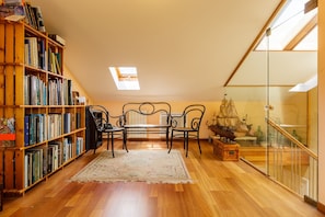 A room with a wooden bookshelf, a table with chairs, a ship model, and a skylight.
