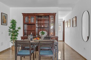 Un comedor con un armario de madera, sillas, una mesa con un jarrón y una planta en maceta.