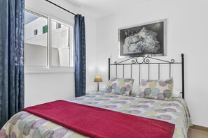 Une chambre à coucher avec un lit, une fenêtre avec des rideaux, un tableau accroché au mur et une lampe de chevet.
