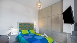 Ein Schlafzimmer mit einem Bett, Nachttischen, einer Lampe, einem Fernseher und einem gemusterten Kopfteil.