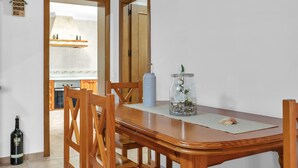 Een eethoek met een houten tafel, stoelen, een vaas met bloemen, een fles en een spiegel aan de muur.
