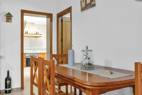 A dining area with a wooden table, chairs, a vase with flowers, a bottle, and a mirror on the wall.