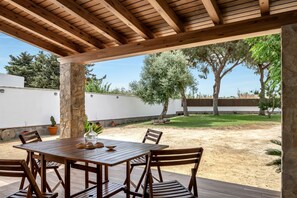 An outdoor patio with a wooden table and chairs, surrounded by stone pillars and potted plants.