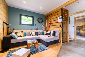 Ein modernes Wohnzimmer mit einem Ecksofa, einem Flachbildfernseher, einer Holzvertäfelung und einer Treppe, die in eine andere Ebene führt.