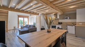 Une cuisine moderne avec des poutres en bois, un coin repas avec une table en bois et un espace de vie comprenant un canapé et un balcon.