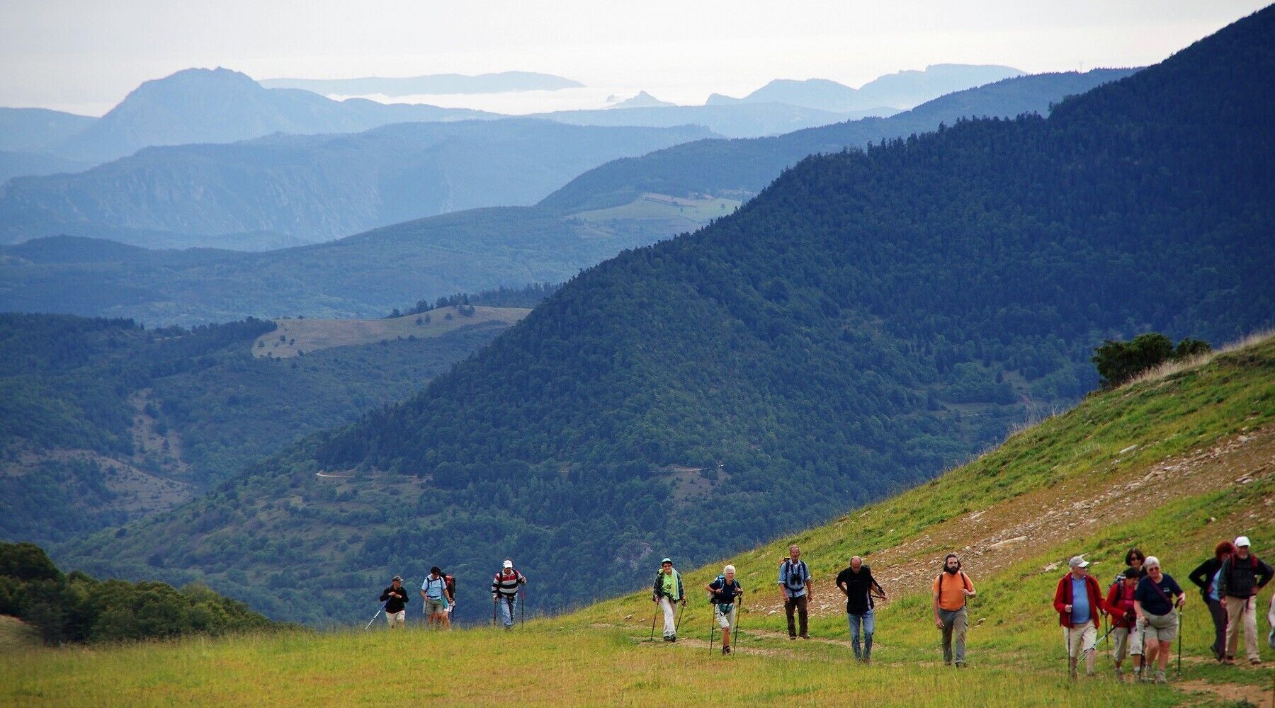 A group of hikers on a grassy hillside with a mountainous landscape in the background.