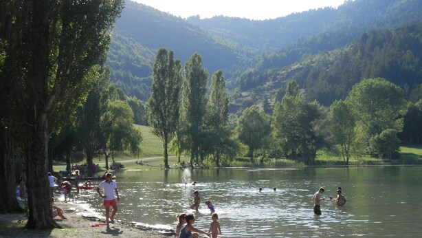 Un paysage au bord d’un lac, où l’on voit des personnes se détendre près de l’eau, avec des arbres et des collines en arrière-plan.