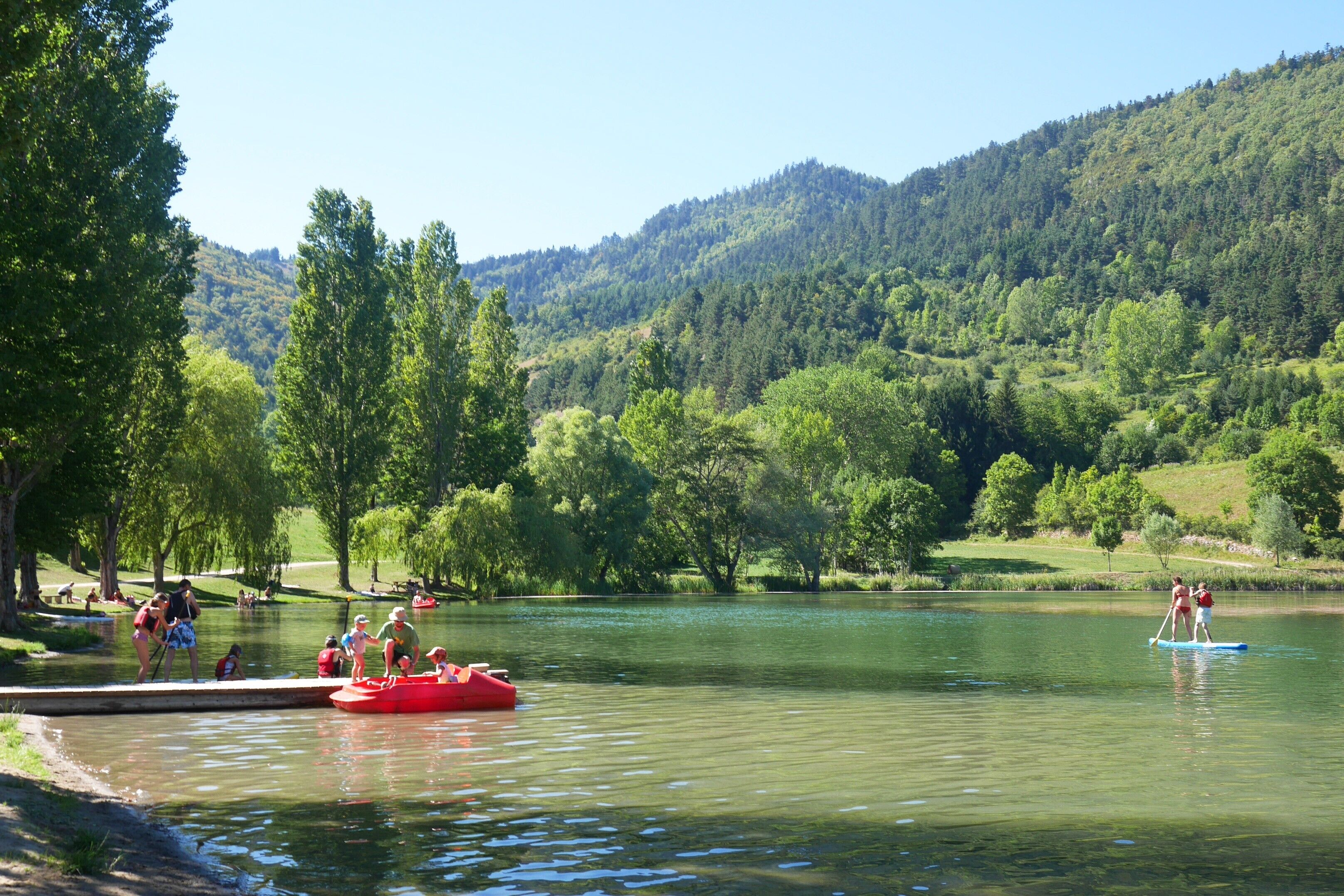 Un lago rodeado de árboles y colinas, con gente disfrutando de actividades acuáticas.