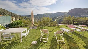 Un espace extérieur aménagé avec une table et des chaises, entouré d’une pelouse bien entretenue et offrant une vue panoramique sur les collines.