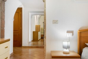 Een slaapkamer met een houten hoofdeinde, een nachtkastje met een lamp, een houten garderobe en een spiegel aan de muur.