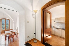 Een eethoek met een tafel en stoelen, een vloerlamp en een uitzicht door een rondboogvormige deuropening naar een keuken.