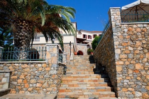Una escalera de piedra que lleva a un edificio con balcón, rodeado de palmeras y un cielo azul despejado.