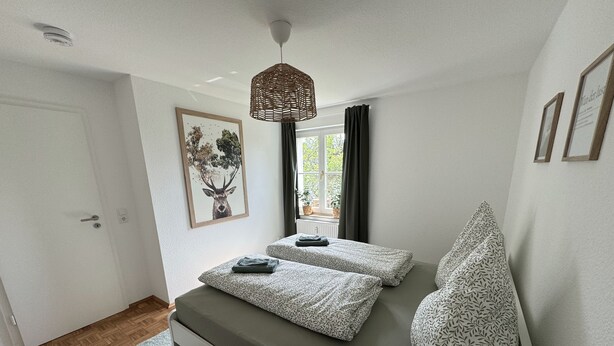 Una camera da letto con un letto, una finestra con tende, una lampada a sospensione e un quadro appeso al muro.