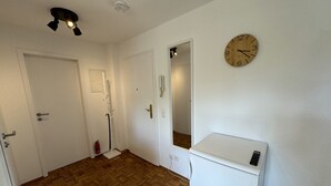Un corridoio con pavimento in legno, pareti bianche, una sveglia ed un elettrodomestico bianco.