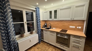 Una cucina moderna con mobili bianchi, un piano di lavoro in legno, forno integrato e una finestra con tende blu.