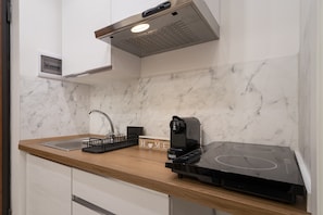 A kitchen with a marble backsplash, a wooden countertop, a coffee maker, and a built-in induction cooktop.