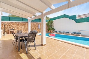 Un'area esterna coperta con piscina, lettini e un tavolo con sedie.
