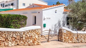 A white building with a stone wall, a tiled roof, and a mailbox. - Villa 'Amber' with Private Pool, Wi-Fi and Air Conditioning (Cala en Porter)