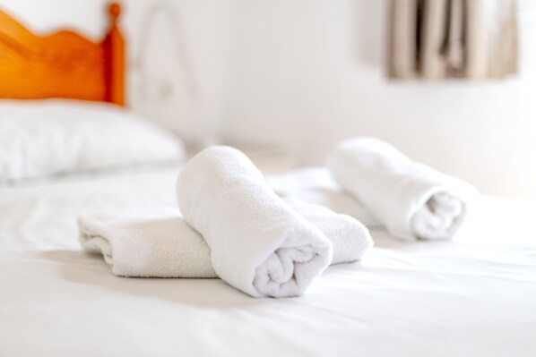 Una cama con sábanas blancas y toallas enrolladas.