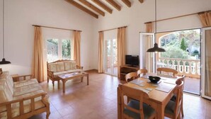 A spacious living area with a wooden ceiling, a sofa, a dining table with chairs, a TV, and a view through a glass door. - Villa 'Diana' with Private Pool, Wi-Fi and Air Conditioning (Cala en Porter)