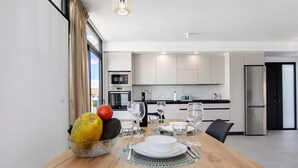 Une cuisine moderne dotée d’appareils électroménagers en acier inoxydable, une table à manger pour deux personnes et une grande fenêtre agrémentée de rideaux.