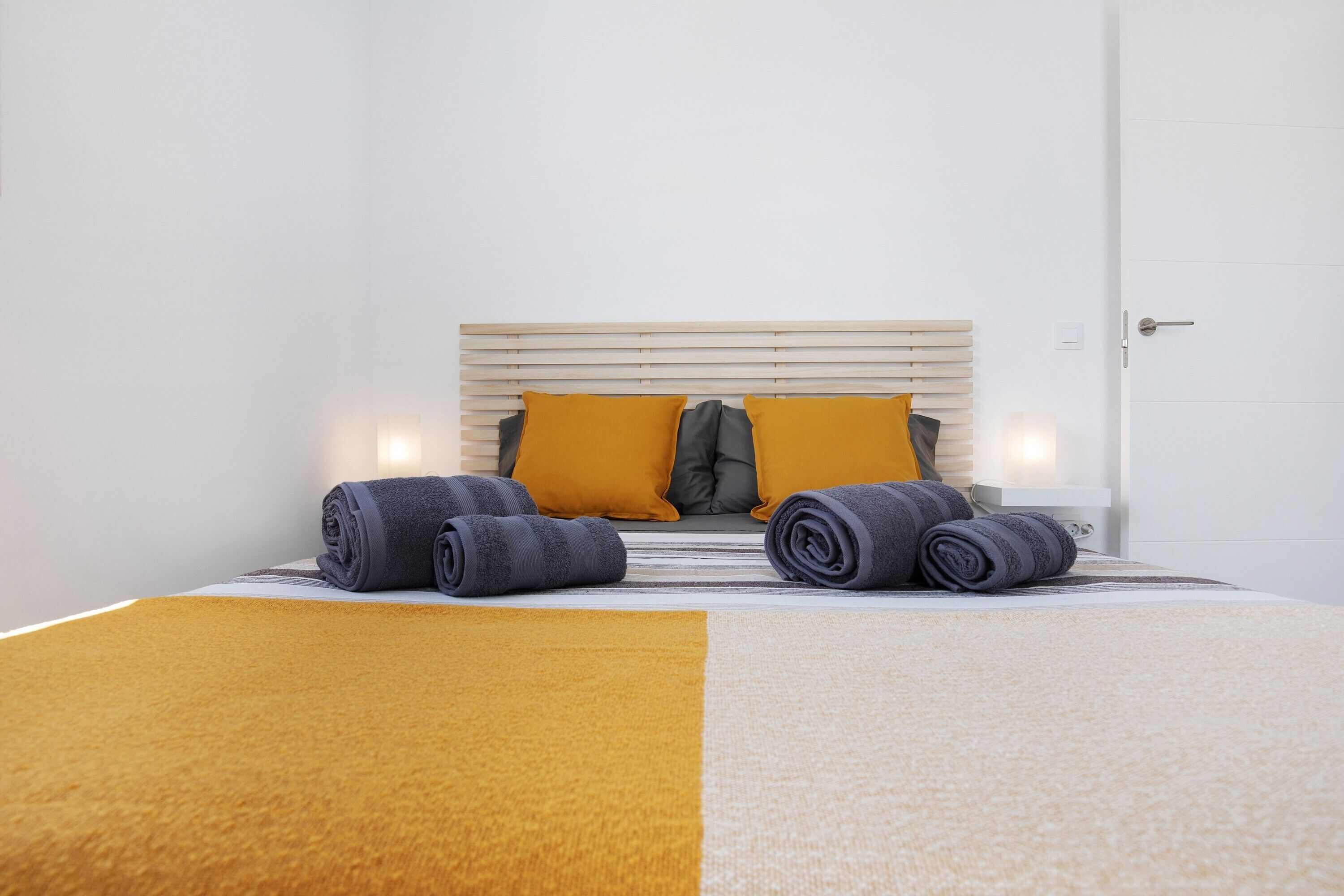 A neatly made bed with a headboard, two pillows, and rolled towels.