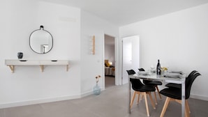 Een moderne eetruimte met een witte tafel, zwarte stoelen en een tafel met glazen blad.