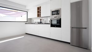 Een moderne keuken met witte kastjes, een roestvrijstalen koelkast, een magnetron en een oven.