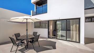 Un patio exterior moderno con una mesa redonda, sillas y un paraguas grande.