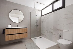 Une salle de bain moderne dotée d’une douche à parois de verre, de toilettes et d’un meuble-lavabo avec un miroir.
