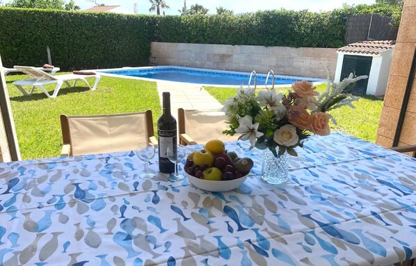Une table placée au bord de la piscine, avec une bouteille de vin, un saladier de fruits et un arrangement floral.