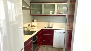 Cocina compacta con refrigerador, horno, lavaplatos y pileta.