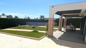 Un patio exterior moderno con piscina, zona de estar cubierta y césped cuidado.
