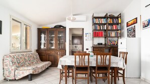 Un comedor con mesa y sillas, un sofá, una estantería y una zona de cocina.