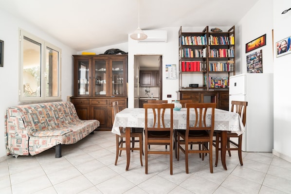 Un espace repas comprenant une table et des chaises, un canapé, une bibliothèque et un coin cuisine.