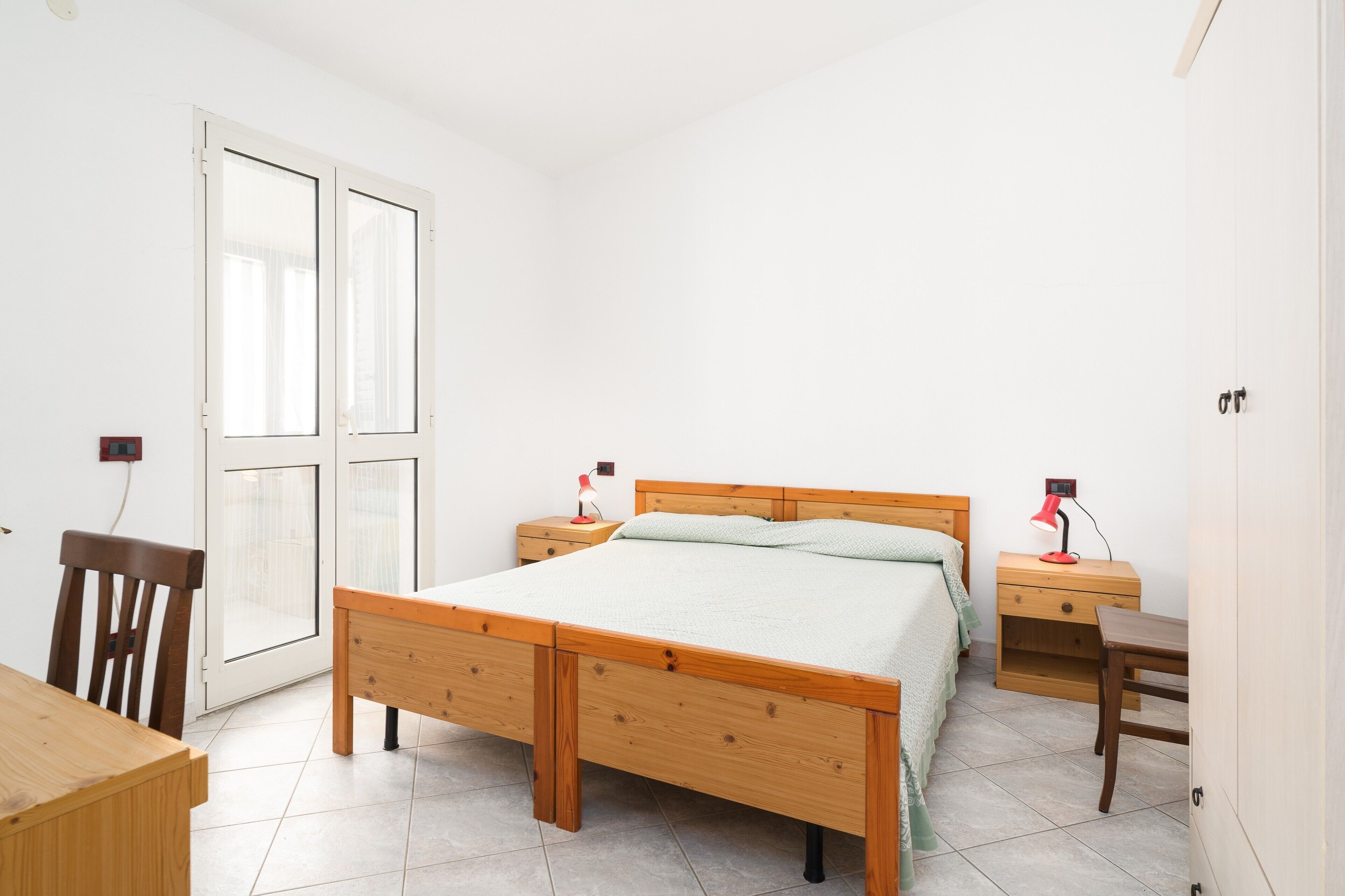 Ein Schlafzimmer mit einem hölzernen Bett, einem Schreibtisch, einem Stuhl, einem Nachttisch mit Lampe und einem Kleiderschrank.